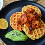 a delicious plate of Cassava corn waffles and shrimp creole with a side of avocado